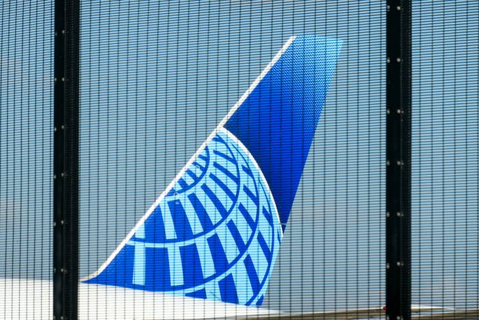 Blue company logo on a grid background, behind a fence