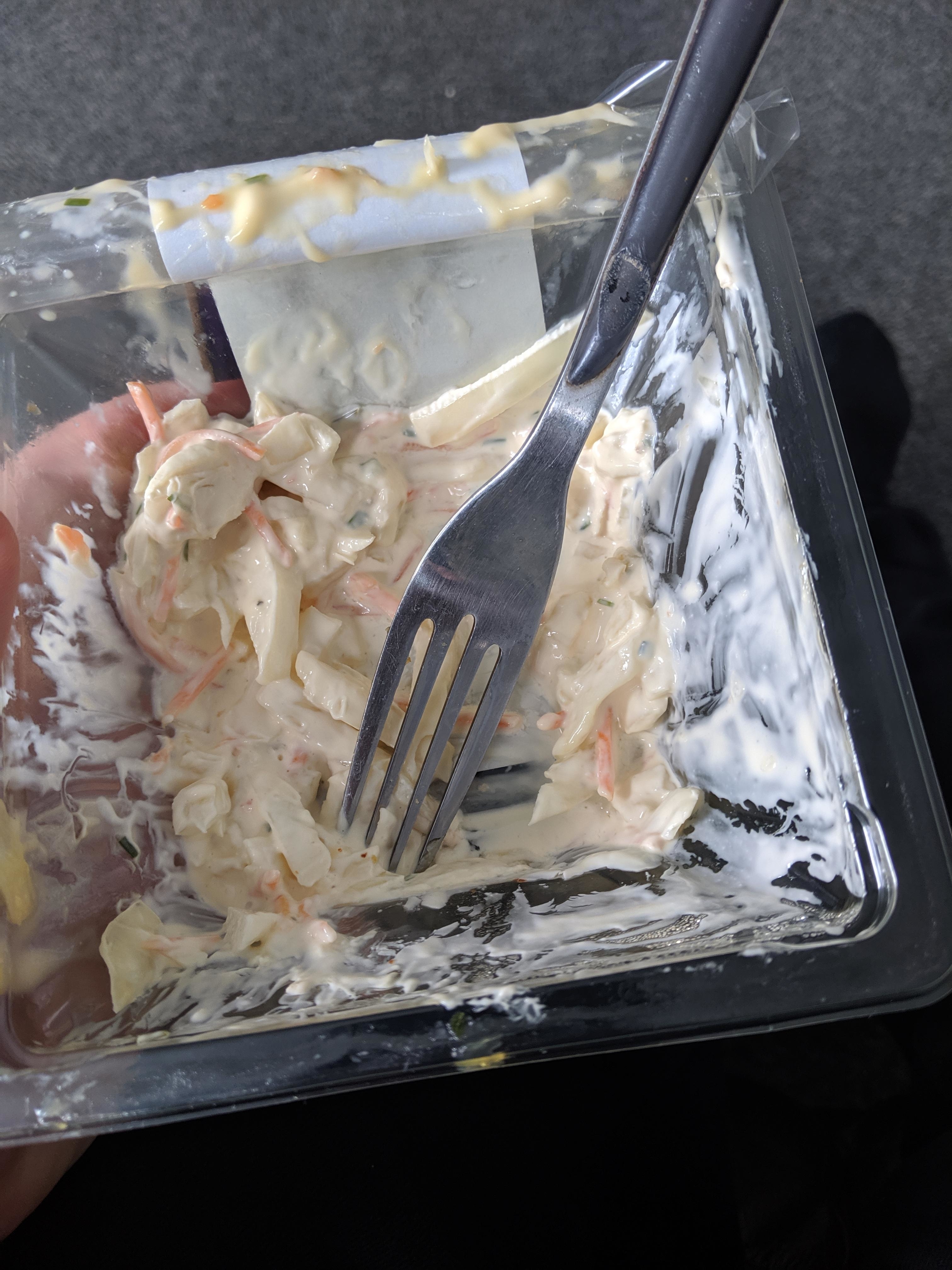 A person holding a plastic container with leftover coleslaw and a fork