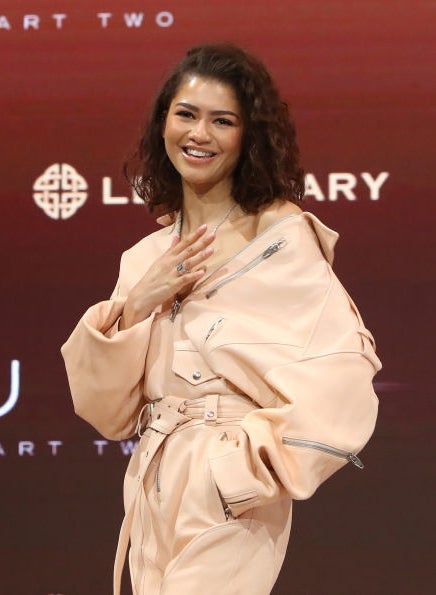 Zendaya in a stylish trench coat at a &#x27;DUNE Part Two&#x27; event, posing with a hand on heart