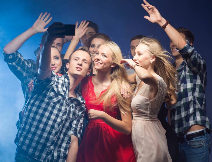 Group of friends taking a selfie, one in a red dress, expressing joy and togetherness