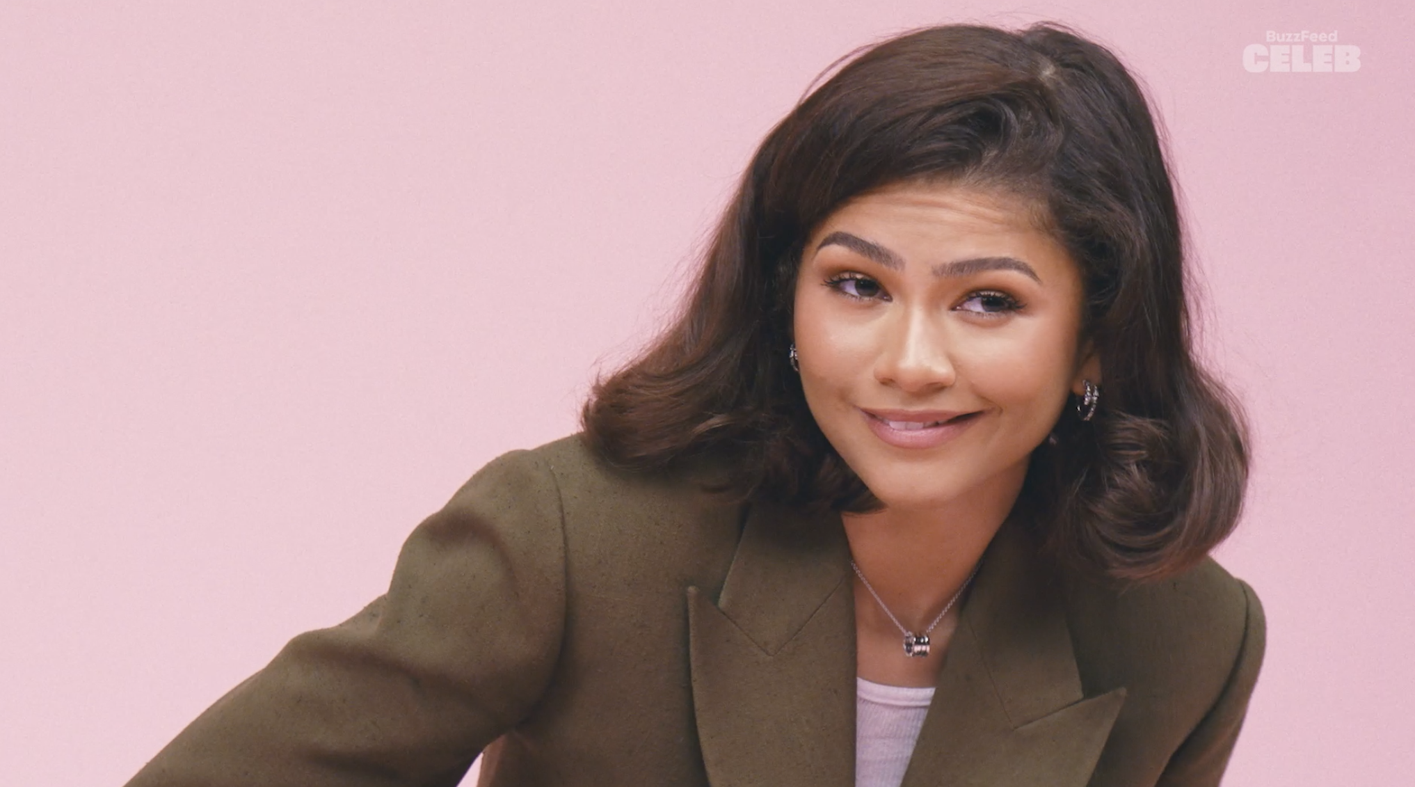 Zendaya smiles, wearing a brown blazer with a necklace, on Buzzfeed Celeb