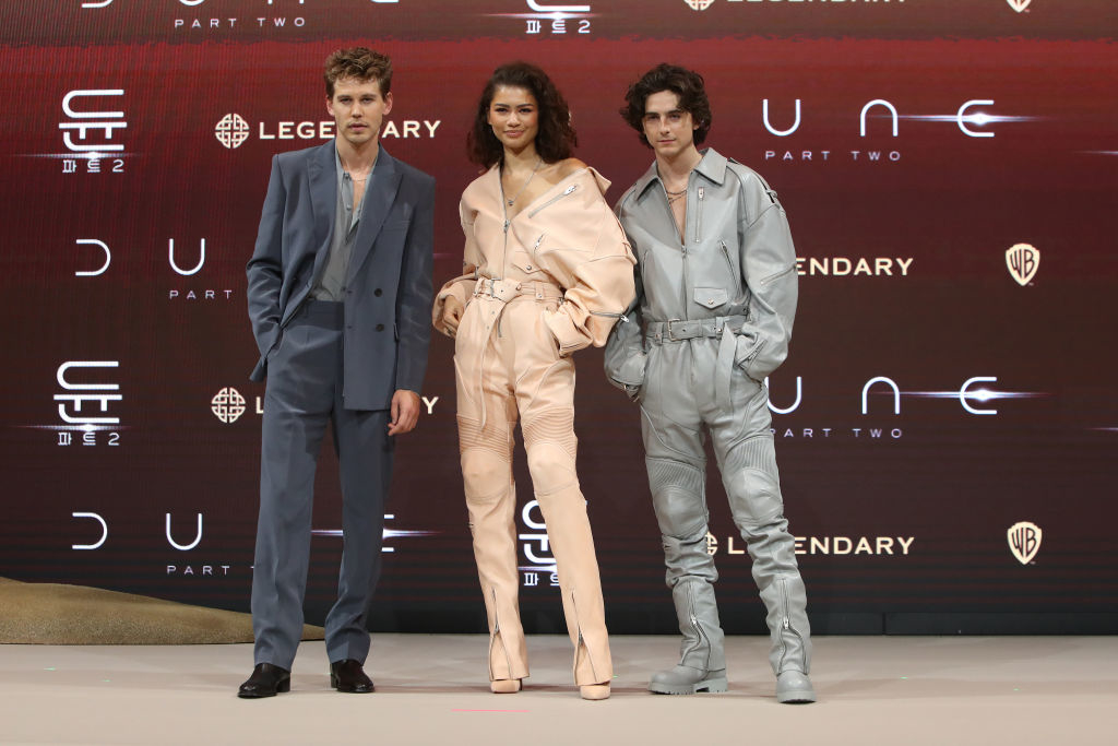 Three actors posing; two men in suits and a woman in a high-waisted outfit, at a film event
