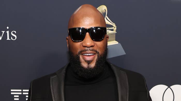 Man in black turtleneck and sunglasses posing on a step and repeat background