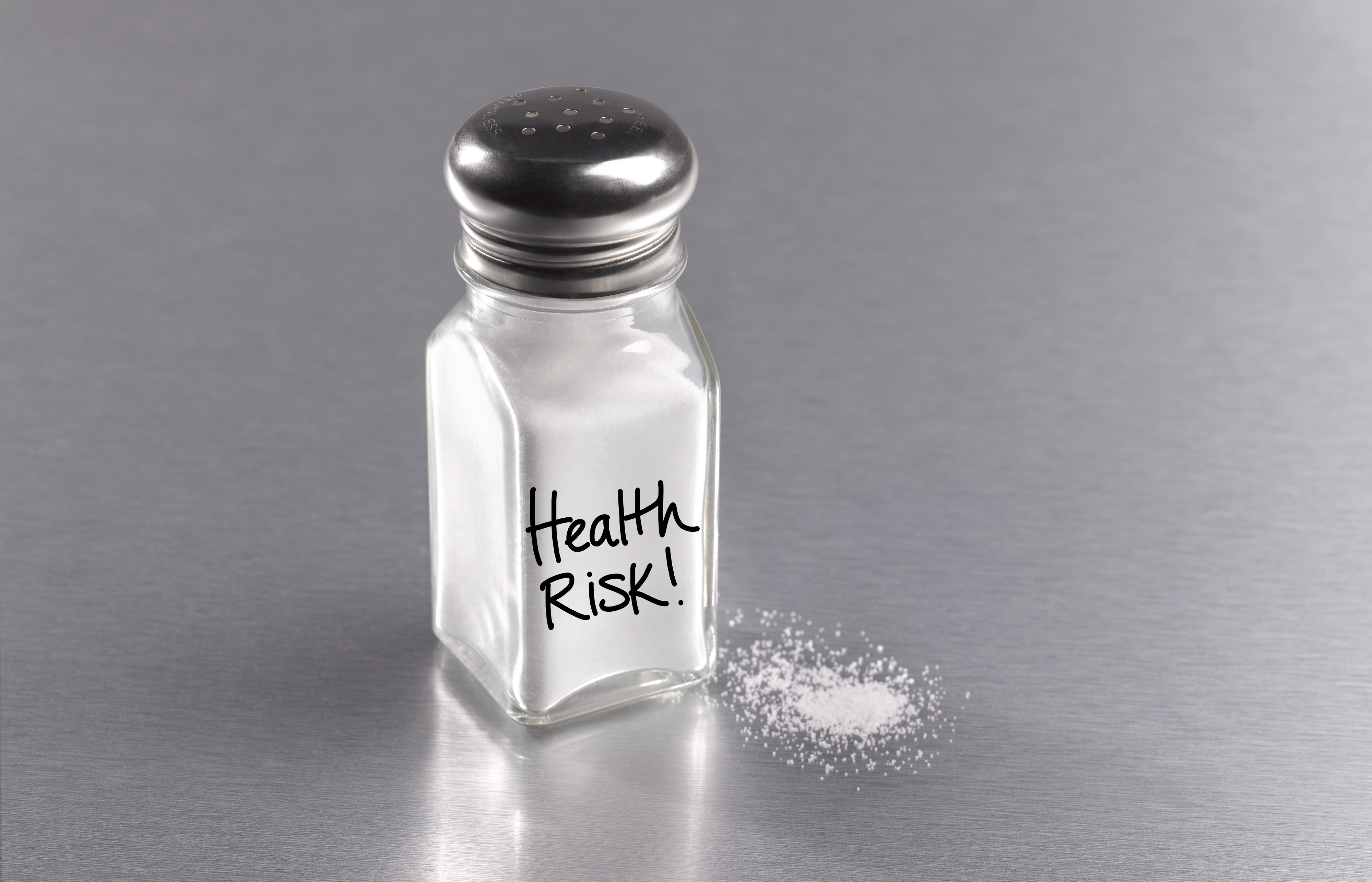 Salt shaker on a table with &quot;Health Risk!&quot; written on it, some salt spilled beside it
