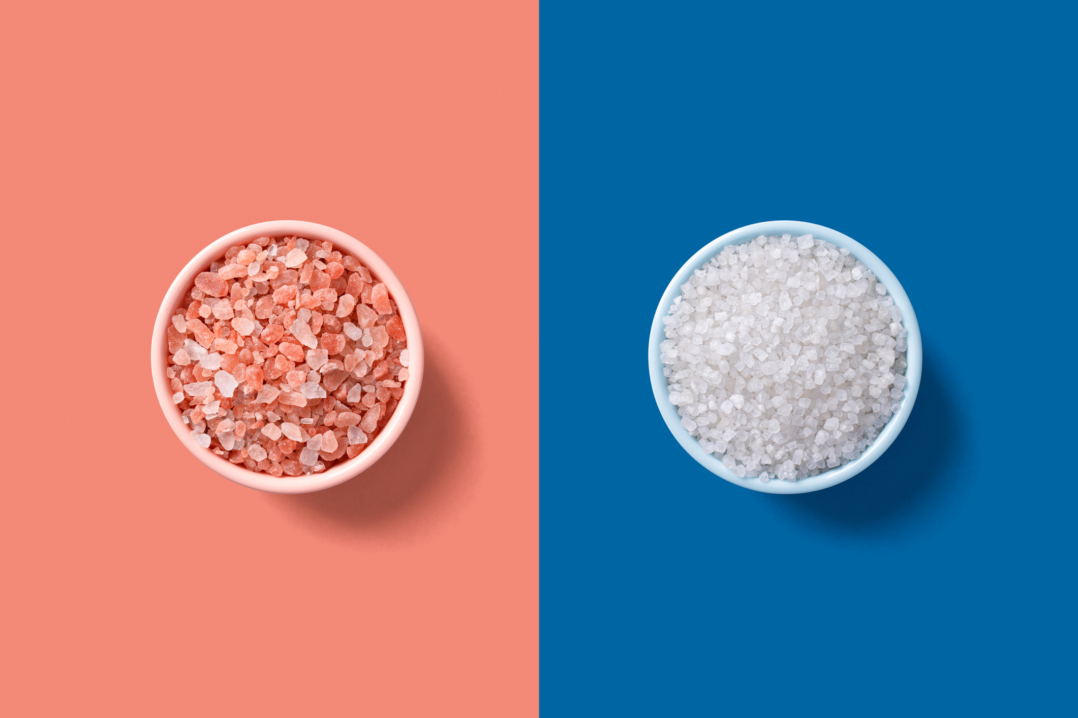 Two bowls of salt, one with pink salt and one with white salt, on split background