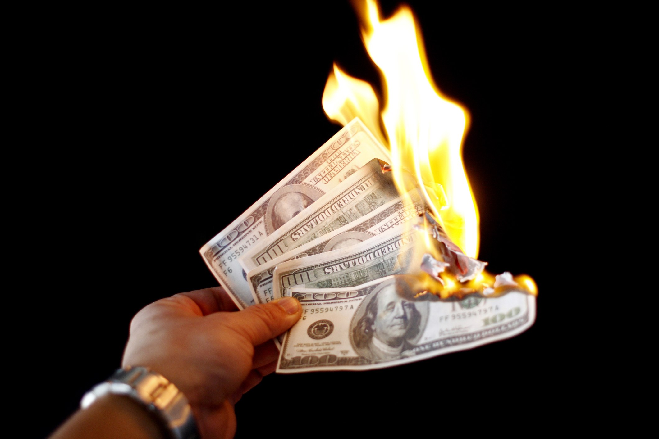 Hand holding cash on fire, symbolizing financial waste or loss, possibly related to parenting expenses