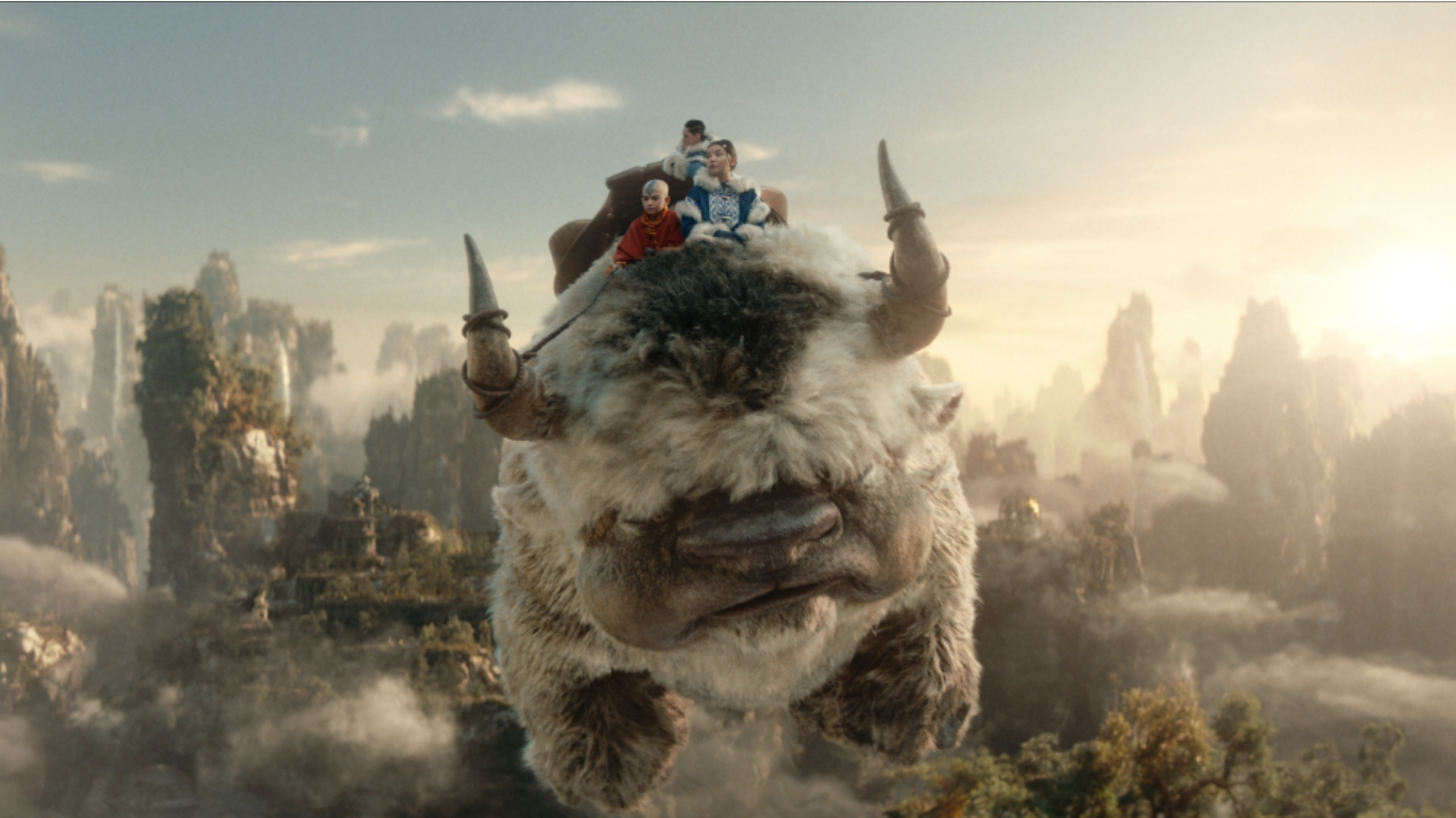 Characters from movie riding a flying beast over a fantastical landscape
