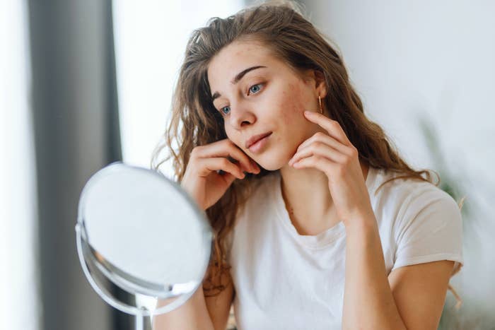 Woman examines her face in a mirror, possibly considering a skincare routine related to the article's food theme