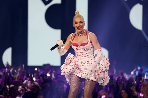 Gwen Stefani performs on stage in a polka dot dress with a layered skirt and fishnet stockings