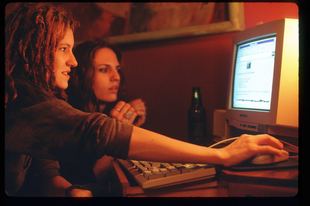 Two individuals intently looking at an old computer screen, vintage setting, possibly exploring early internet content