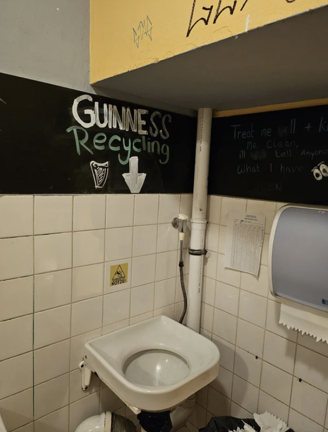 A restroom with a humorous sign &quot;GUINNESS RECYCLING&quot; pointing to a throwup sink