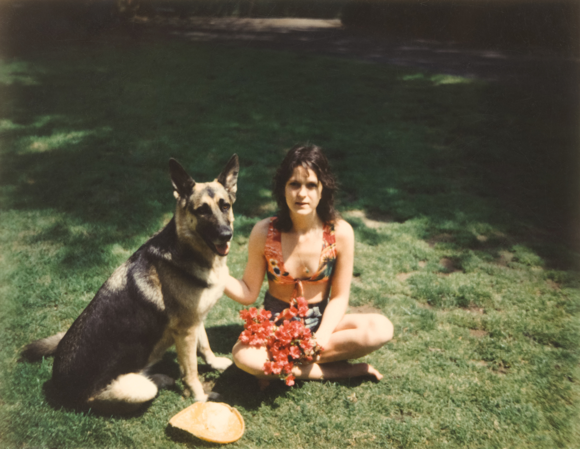 Woman in a floral dress sitting with a German shepherd on grass, both posing for the camera