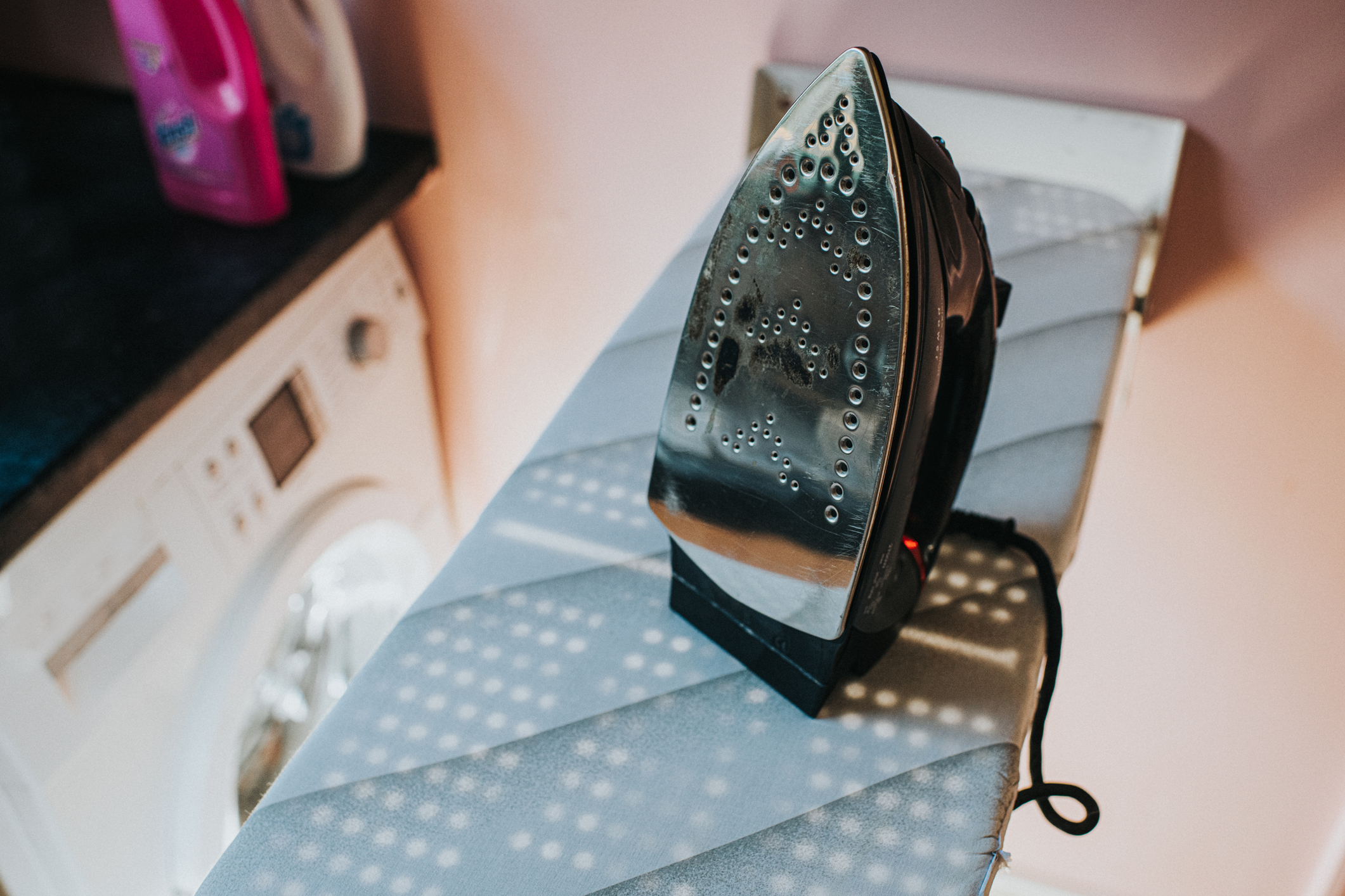 An iron on an ironing board with a washing machine in the background