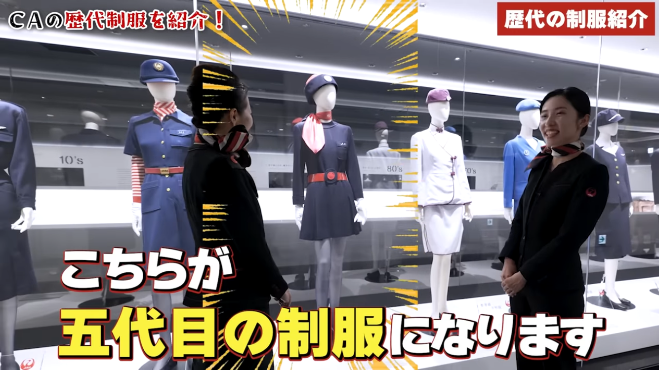制服を展示するショーケースの前で笑顔の女性が立っています。