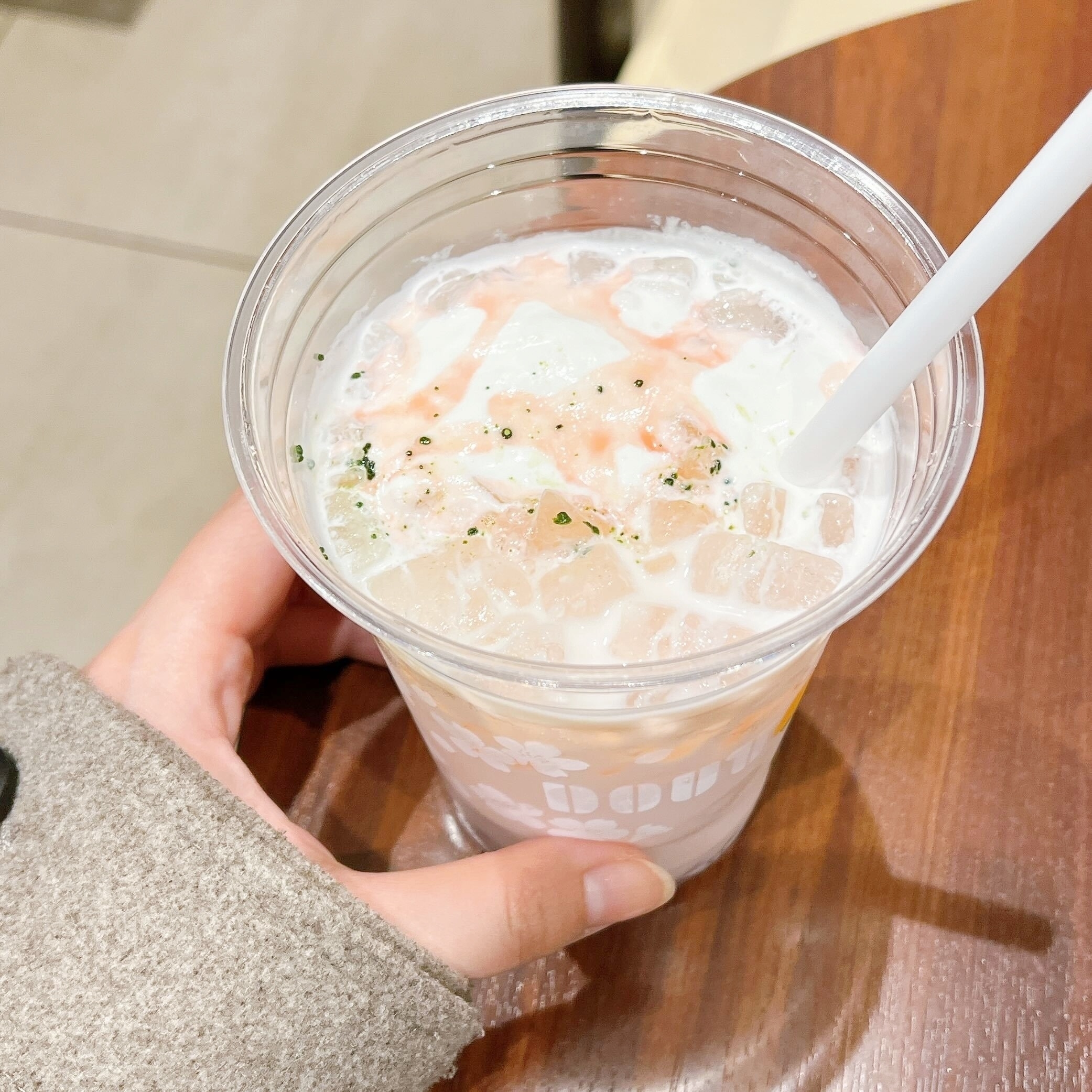 手がプラスチックカップのドリンクを持っていて、ストローが刺さっています。