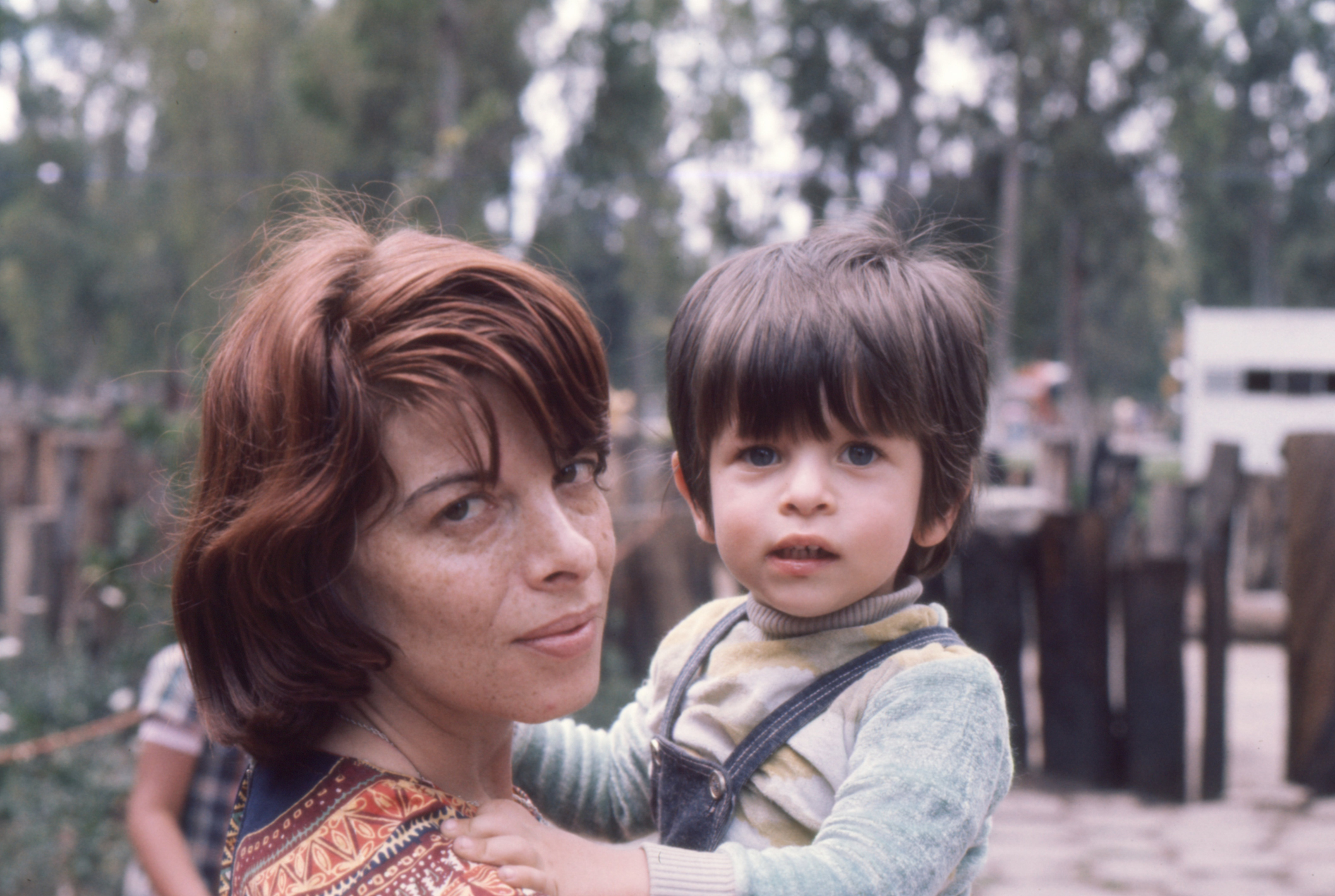 Woman holding young child, both looking at the camera with a natural backdrop