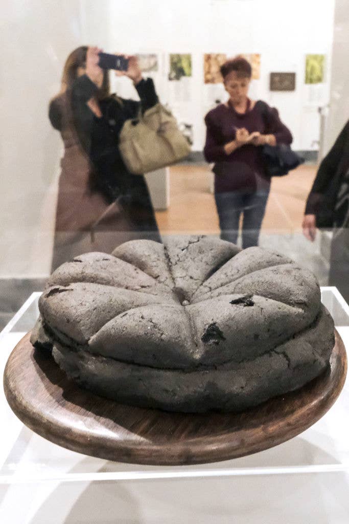 Art exhibit featuring a sculpture resembling a loaf of bread, with visitors observing in the background