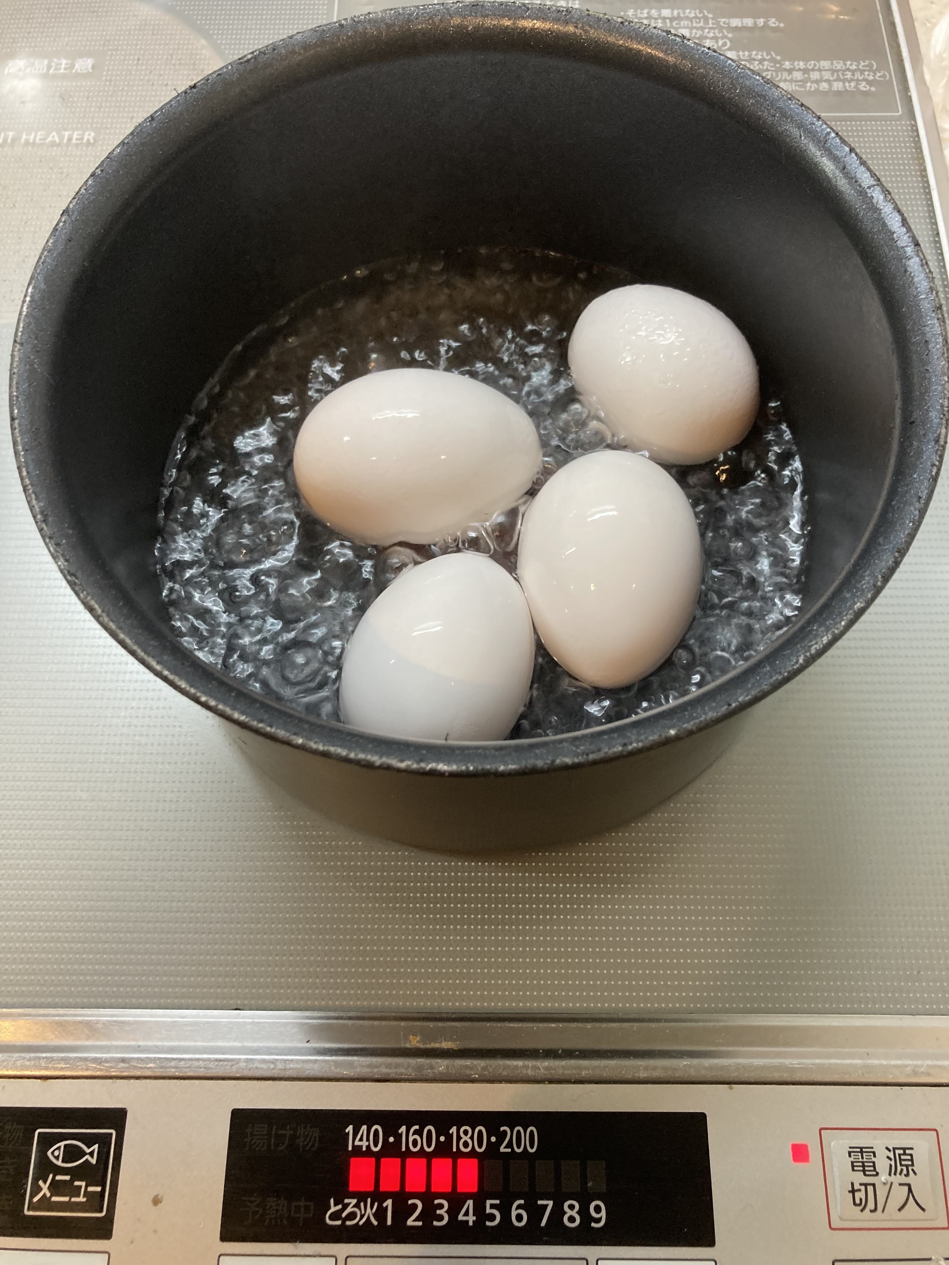 鍋で茹でている卵が5つあり、前面には温度設定表示がある。