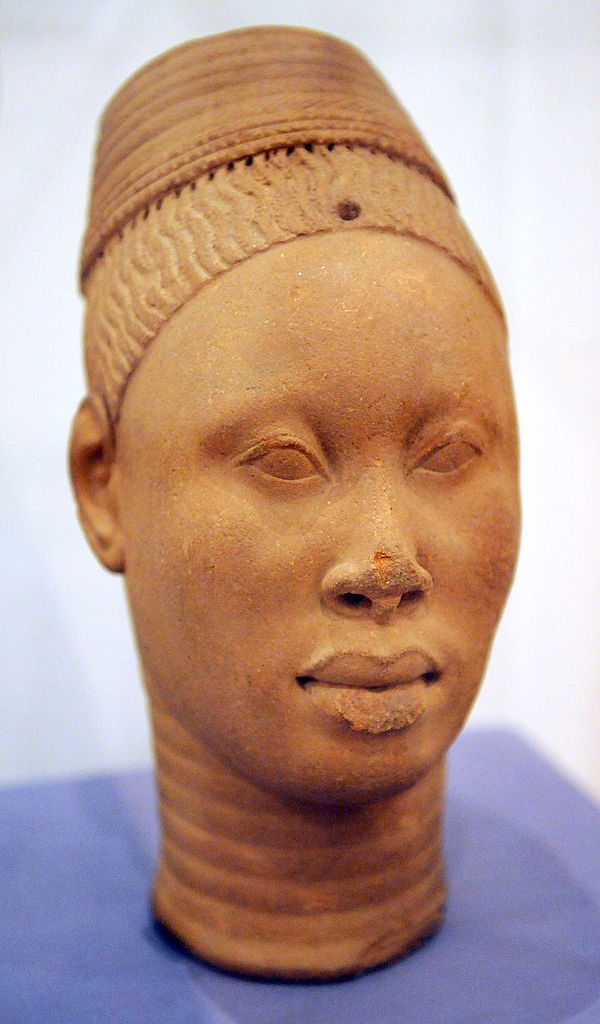 Ancient terracotta sculpture of a human head with intricate hair details, displayed against a plain background