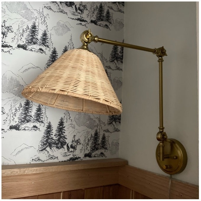 Wall-mounted brass lamp with a wicker shade in a room with wallpaper
