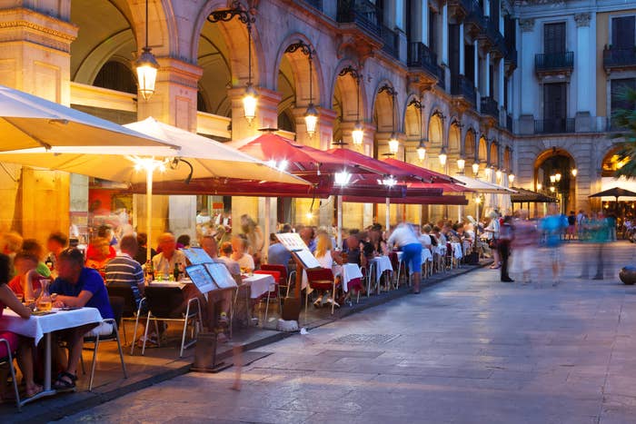 Outdoor café with patrons dining and walking in a European city&#x27;s square at dusk