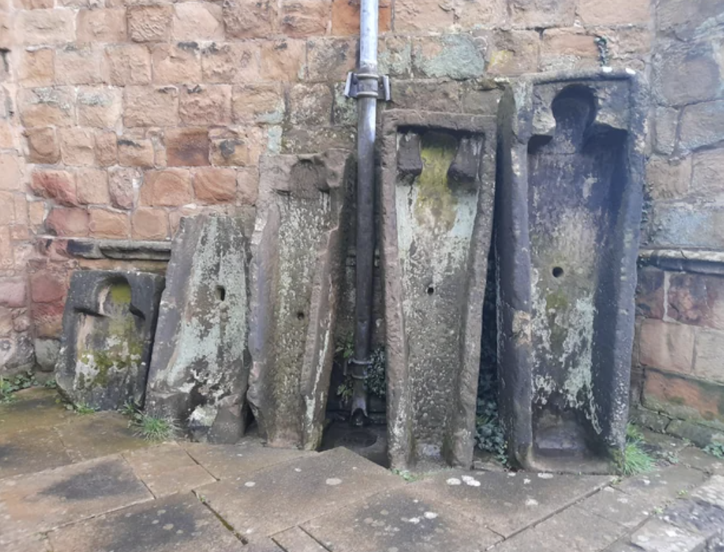 Ancient stone stocks used for public punishment next to a brick wall, no people present