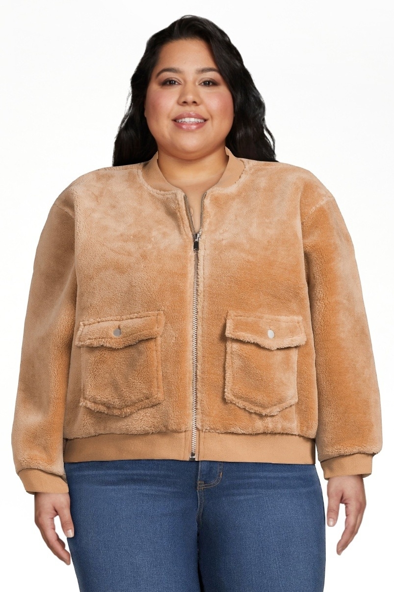 model in a faux fur jacket and jeans, standing, with a smiling expression