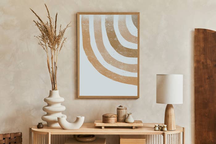 Geometric abstract art hangs above a console table with decorative vases and a lamp in an interior setting