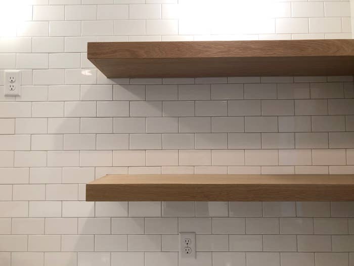 Two wooden shelves on a white subway tile wall with electrical outlets below them