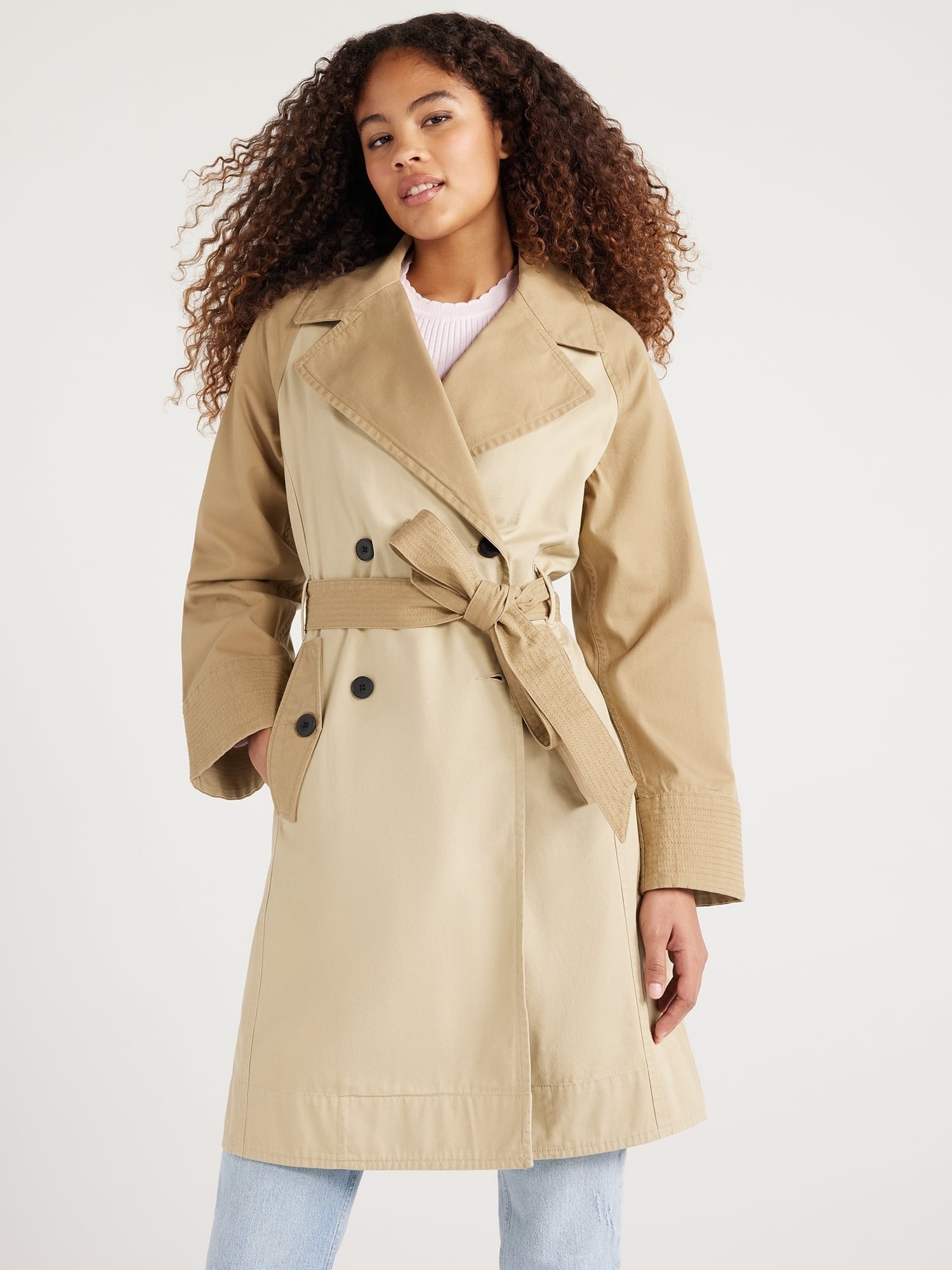 A model wearing a classic trench coat with a belt and button details, paired with jeans