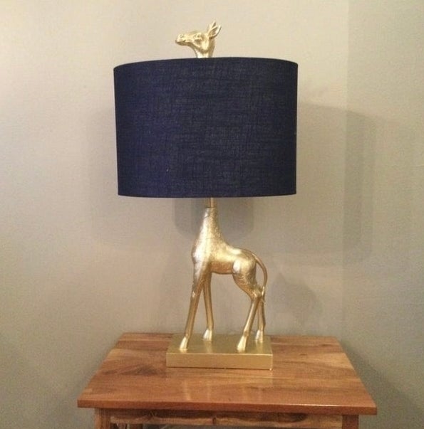 Gold giraffe lamp base with a navy lampshade on a wooden table.