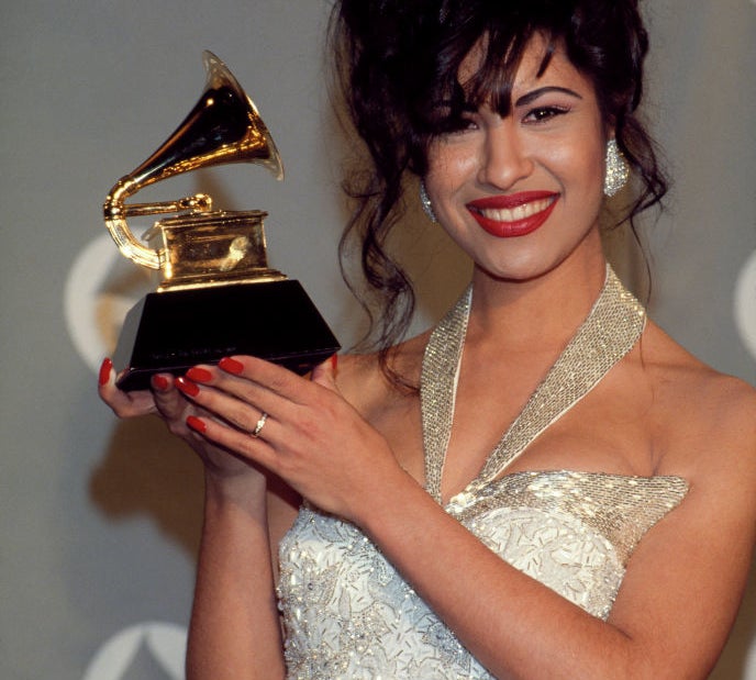 Woman holding a Grammy Award, wearing a sequined gown with spaghetti straps