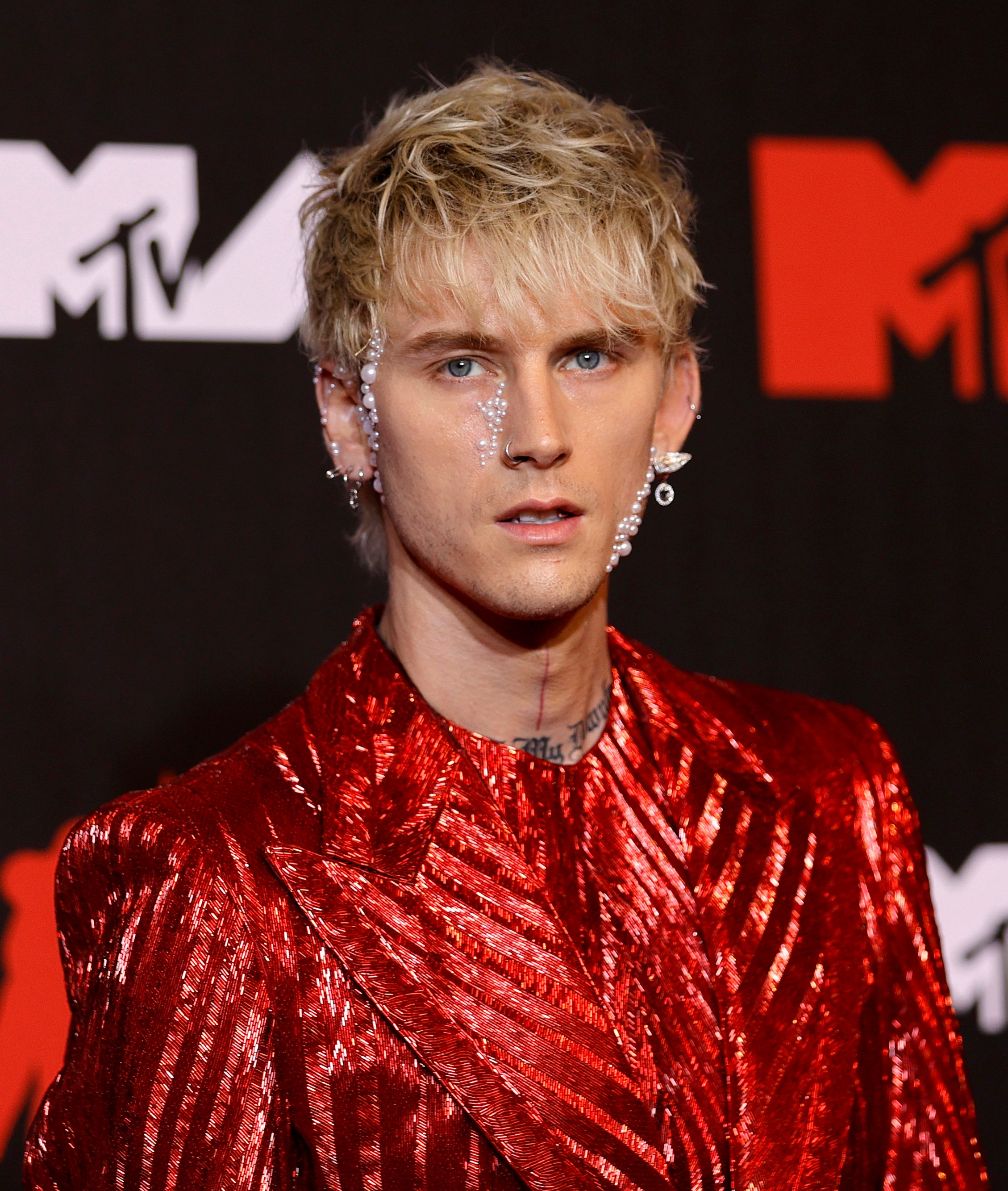 MGK in a shiny red jacket poses on the MTV event backdrop