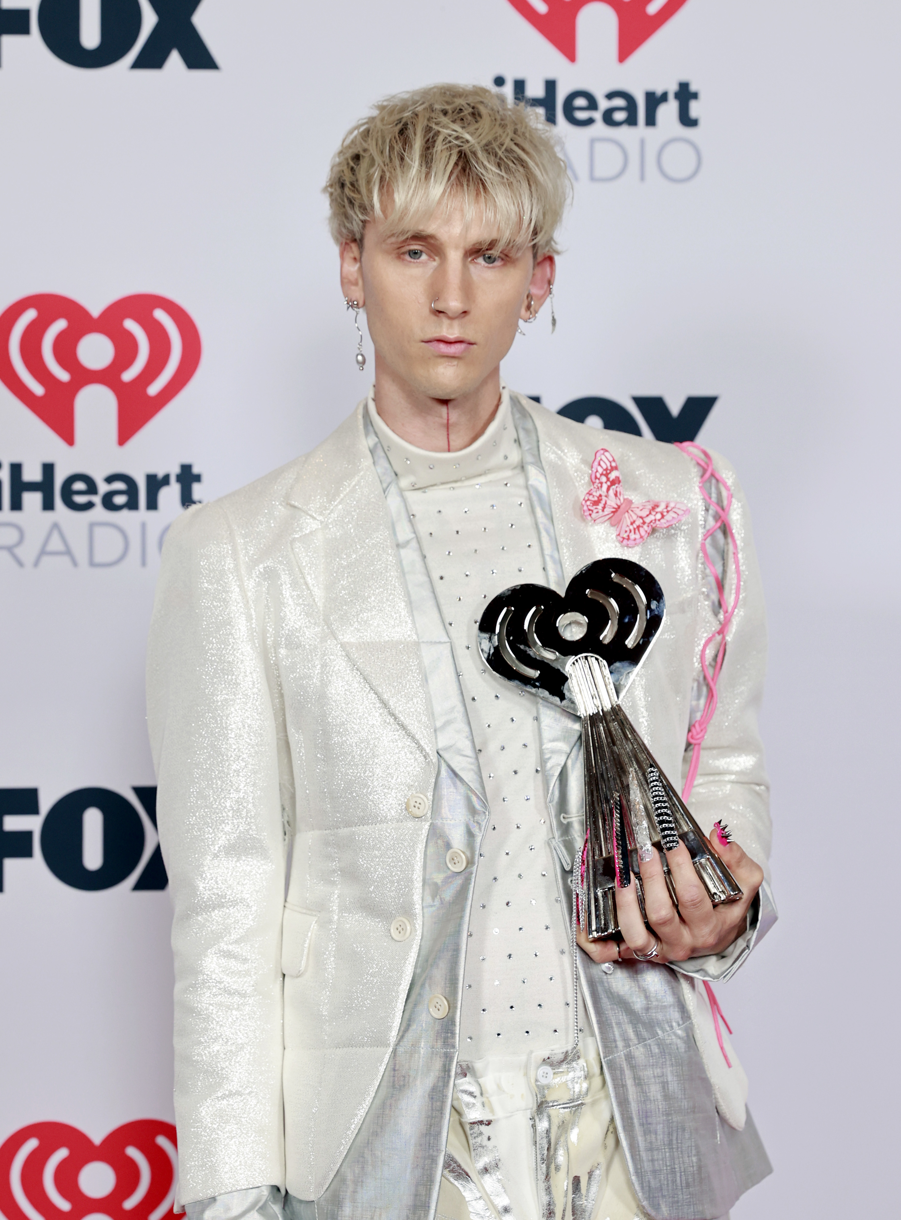 Machine Gun Kelly in a silver patterned suit holding an award