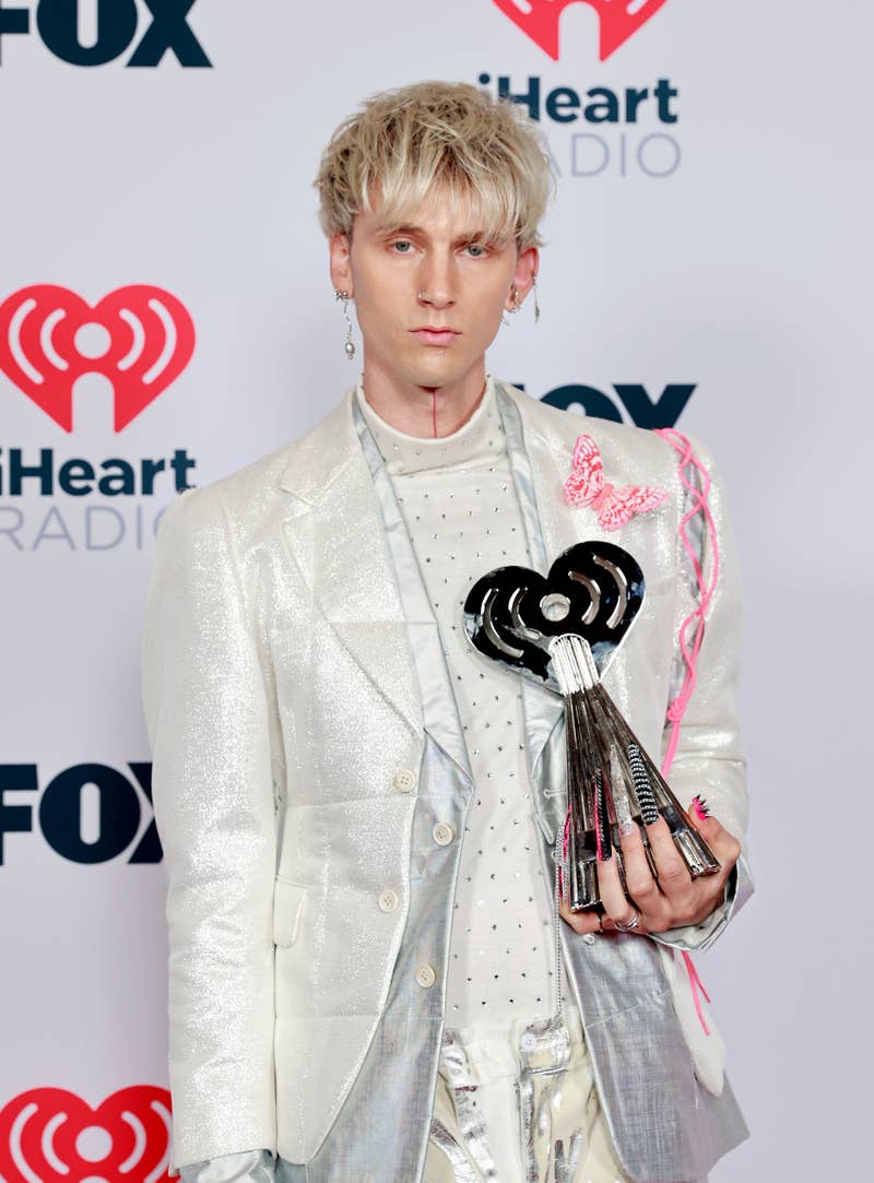 Machine Gun Kelly in a silver patterned suit holding an award