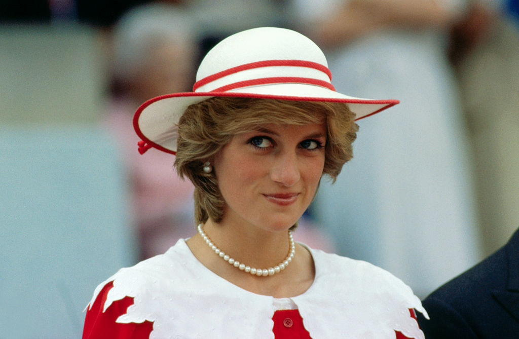Princess Diana wears a white dress with red trim and a wide-brimmed hat at an event