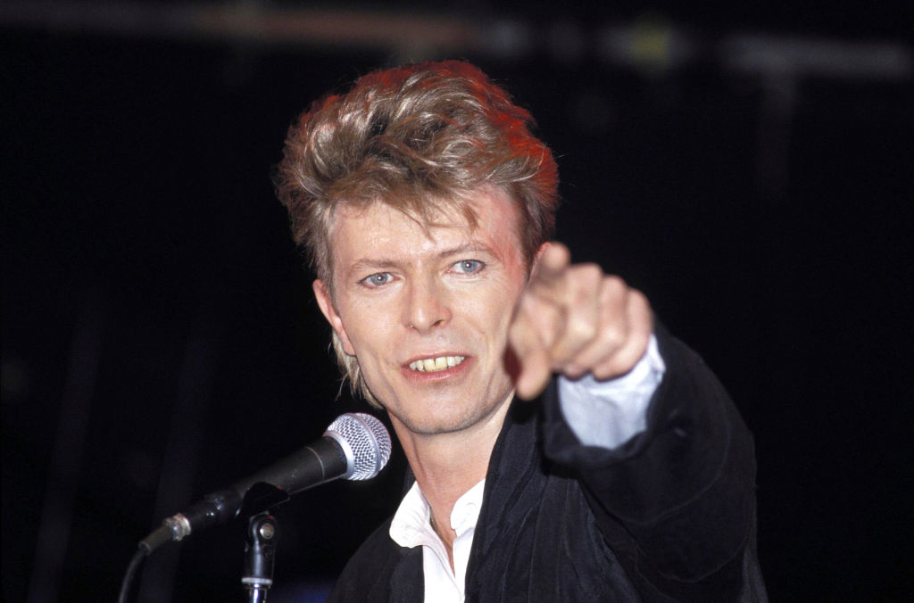 David Bowie in a suit, pointing, with a microphone in front