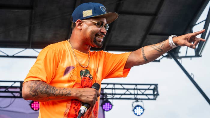 Juvenile on stage performing with microphone, wearing an orange shirt and a blue cap