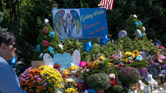 Memorial site with photo of Gabby Petito and &quot;Forever in our hearts&quot; text, surrounded by flowers and tributes