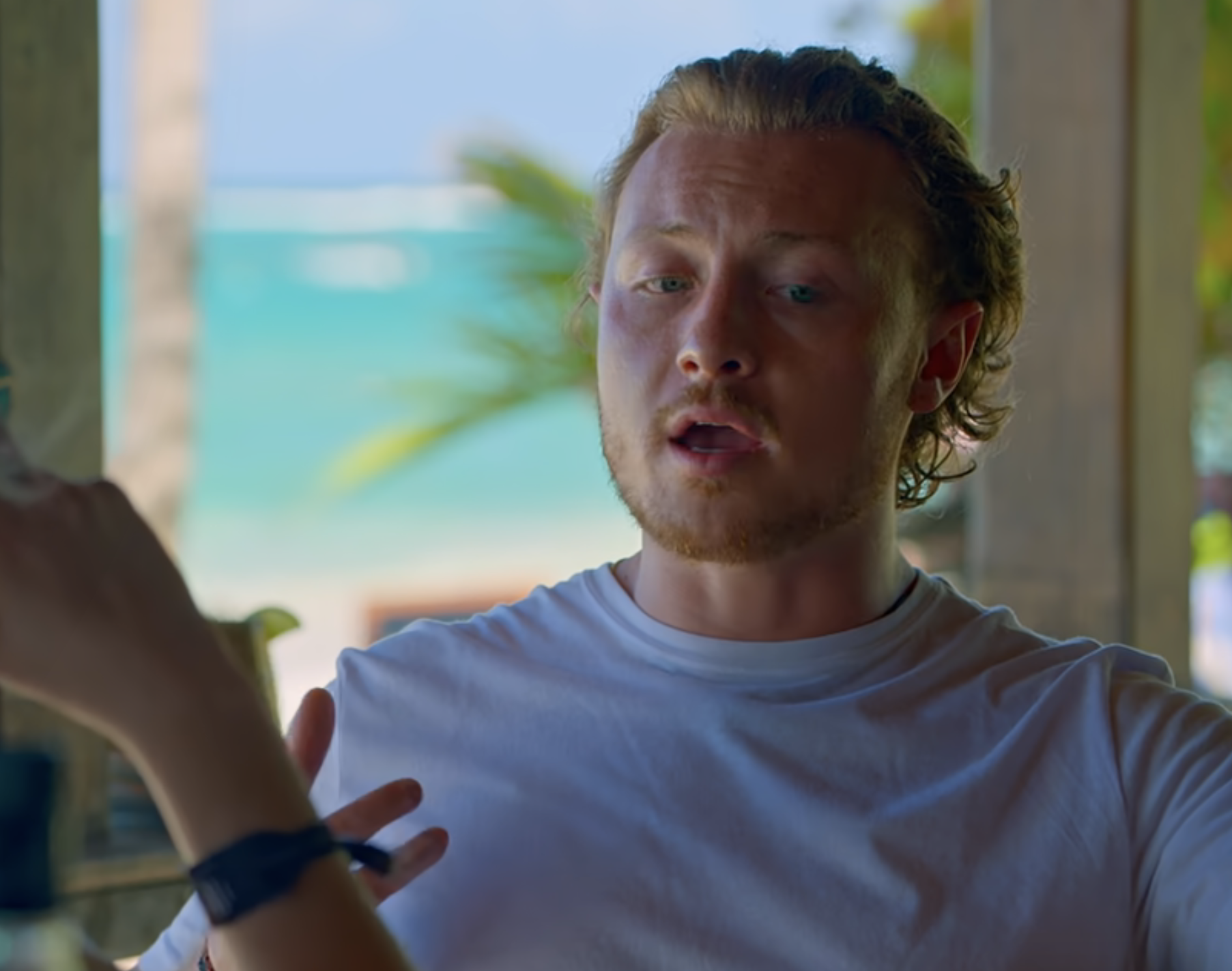 Man in a conversation with a woman whose face is unseen, in a room with a view of the outdoors. Warnings for sex, language, sex references shown