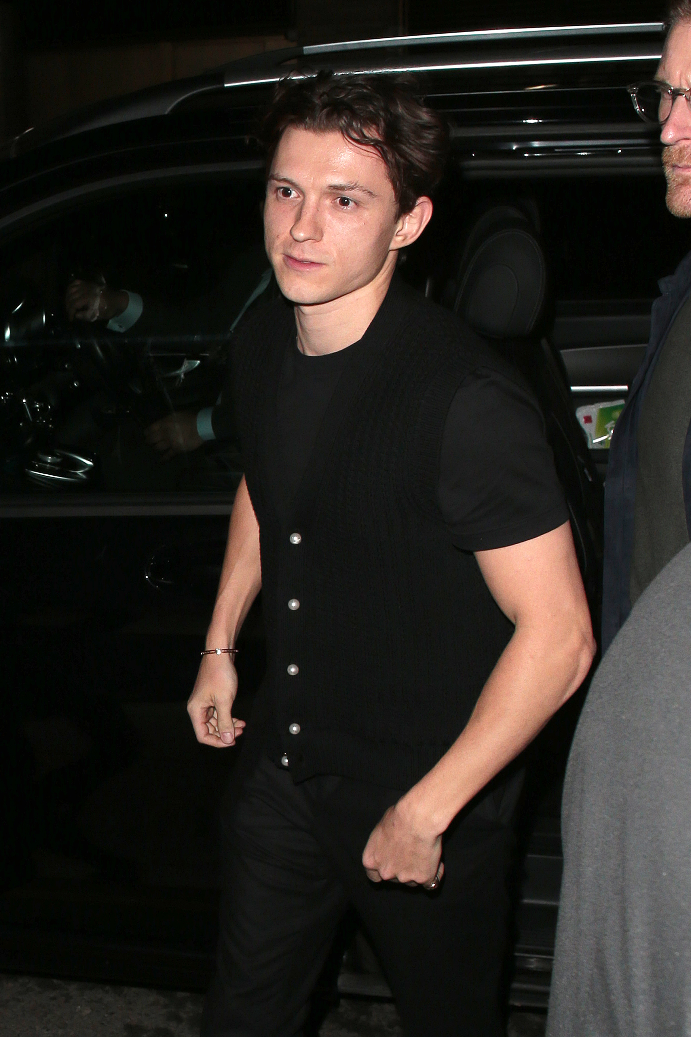 Tom Holland in a casual sleeveless top and trousers, exiting a vehicle