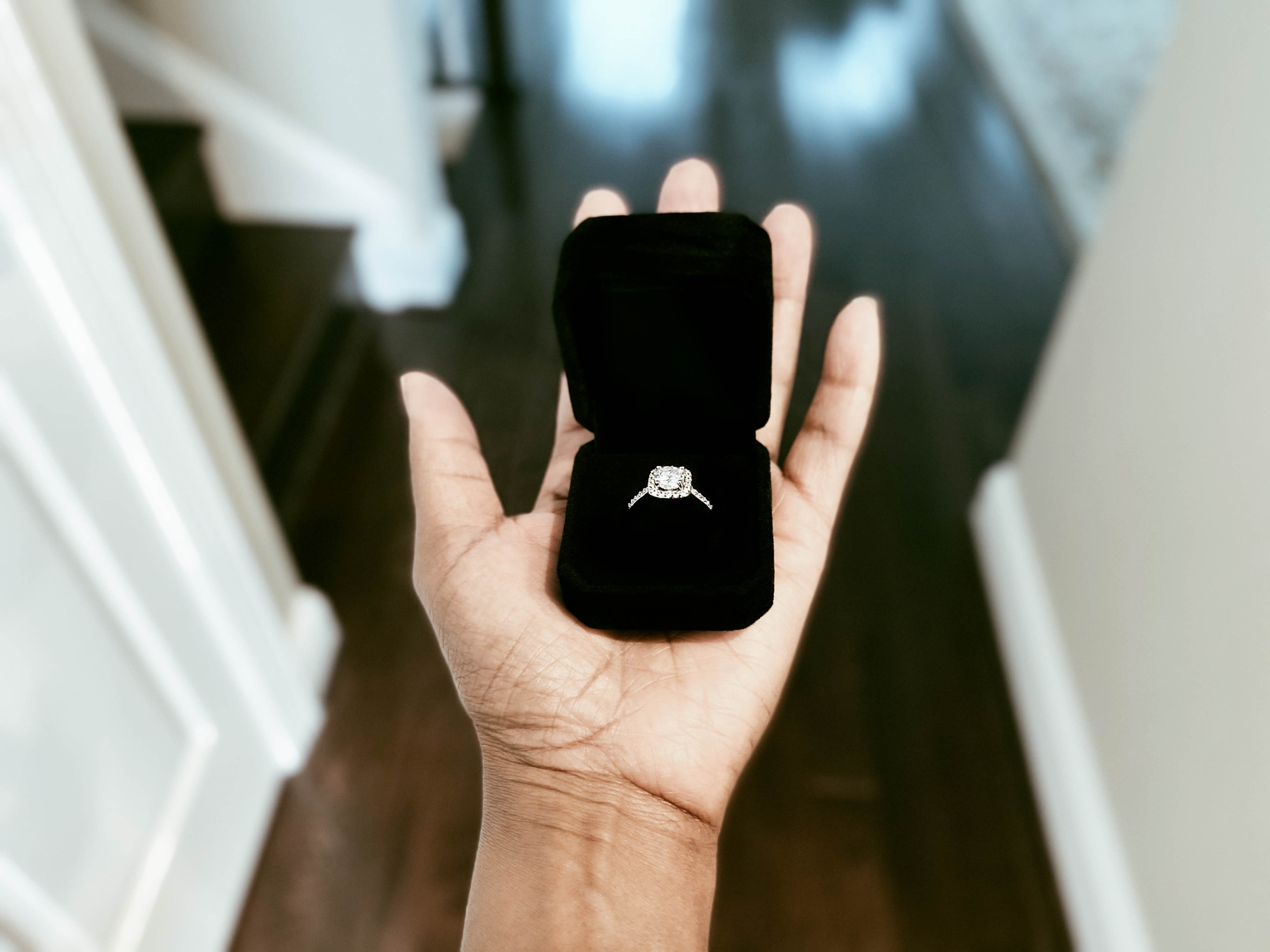 Person&#x27;s hand holds an open ring box with an engagement ring inside, indoors
