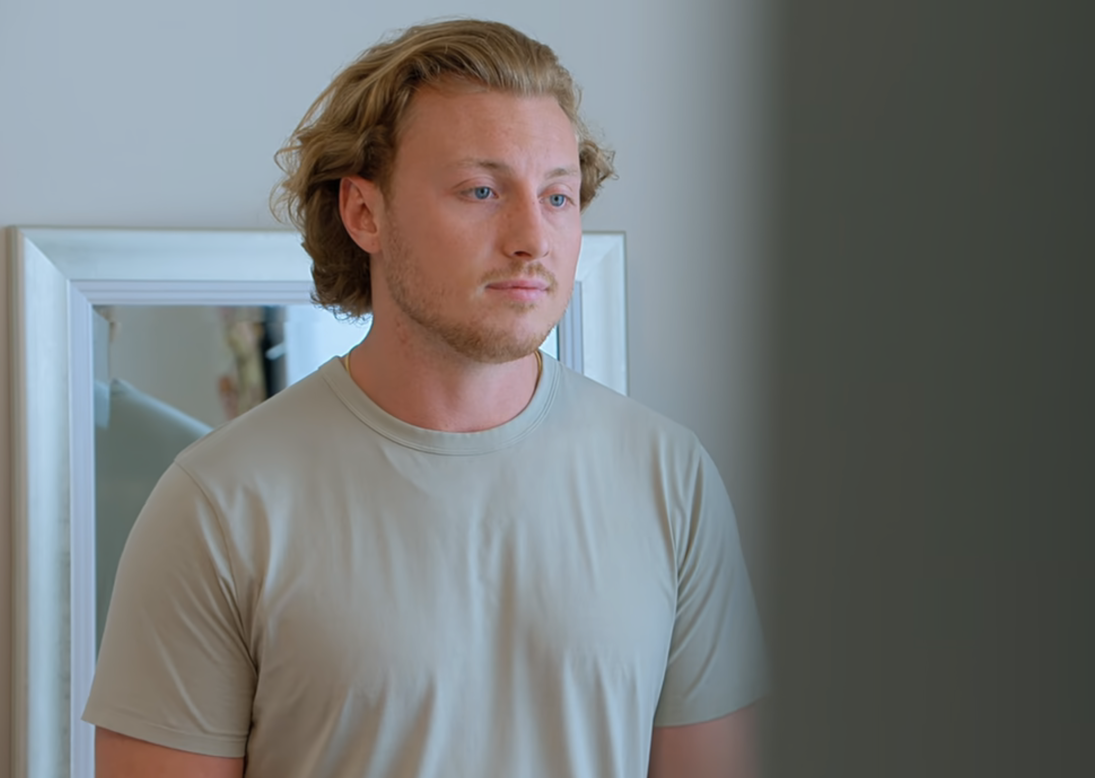 Man in a t-shirt looking at his reflection in a mirror with a concerned expression