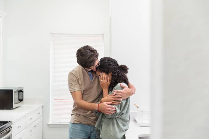 A couple embrace in a kitchen, displaying a moment of affection or comfort