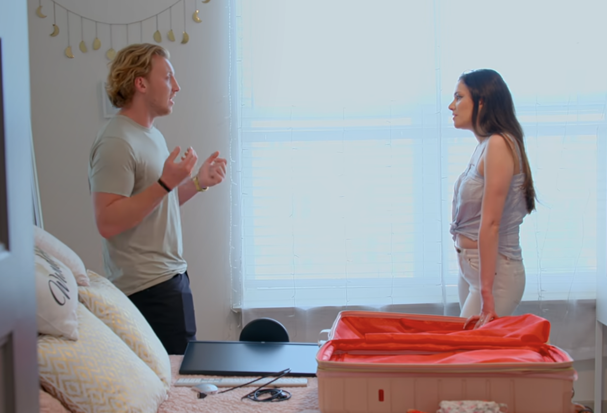 Two people having a conversation by an open suitcase in a bedroom