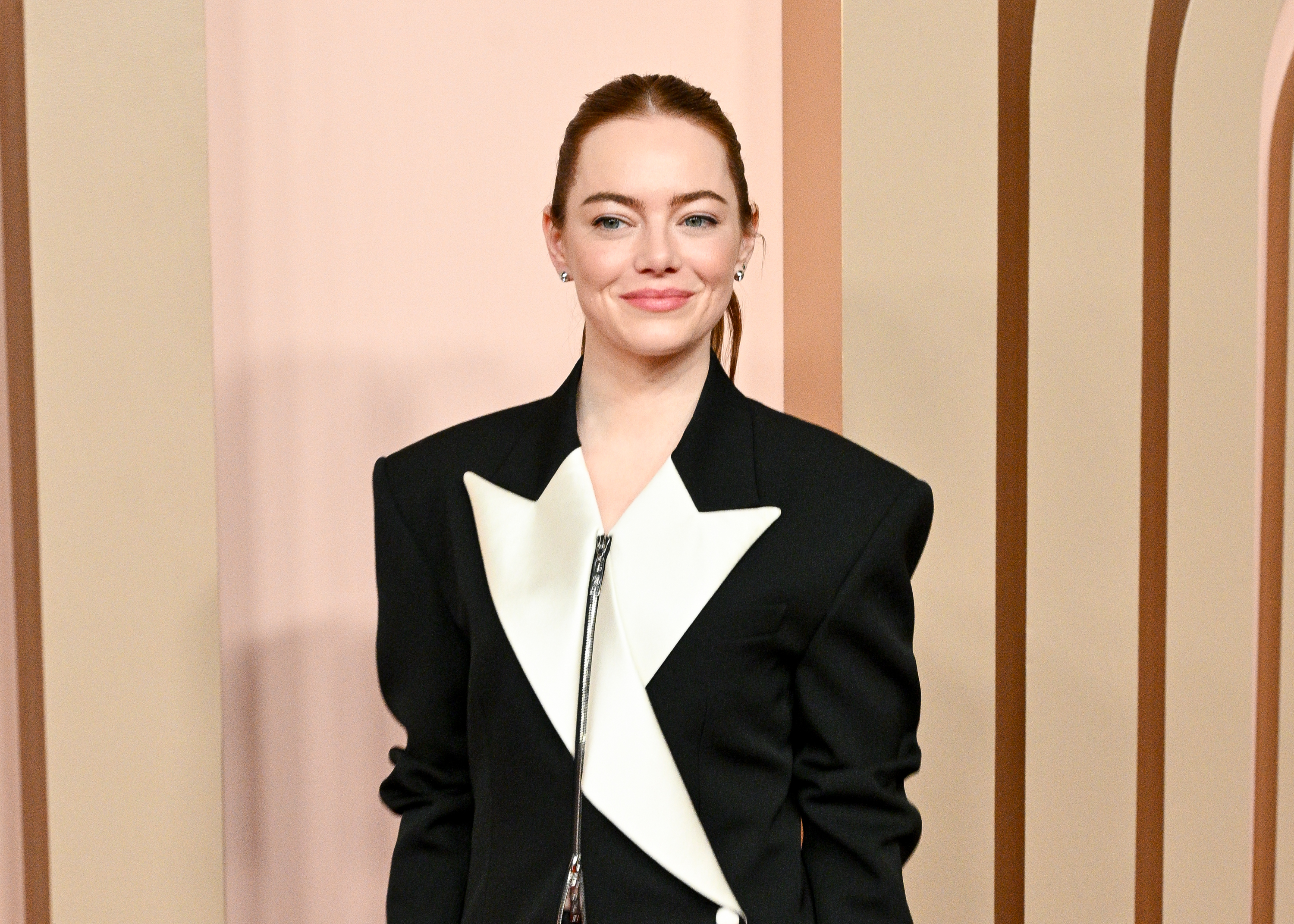 Emma Stone in a black jacket with an oversized white lapel, smiling at the camera