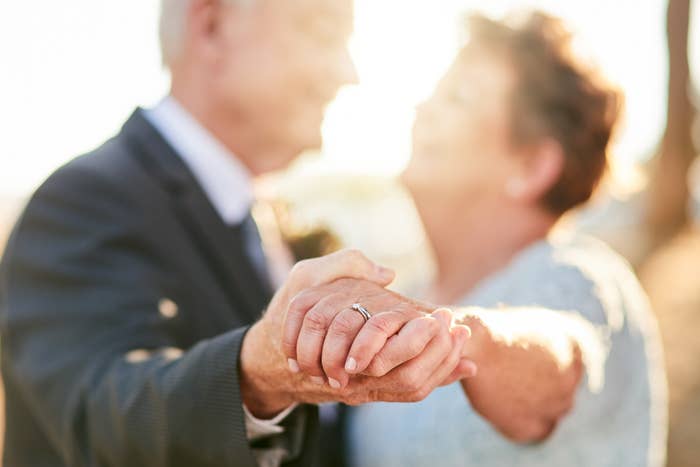 Elderly couple holding hands, smiling, with focus on their interlocked hands showcasing wedding rings