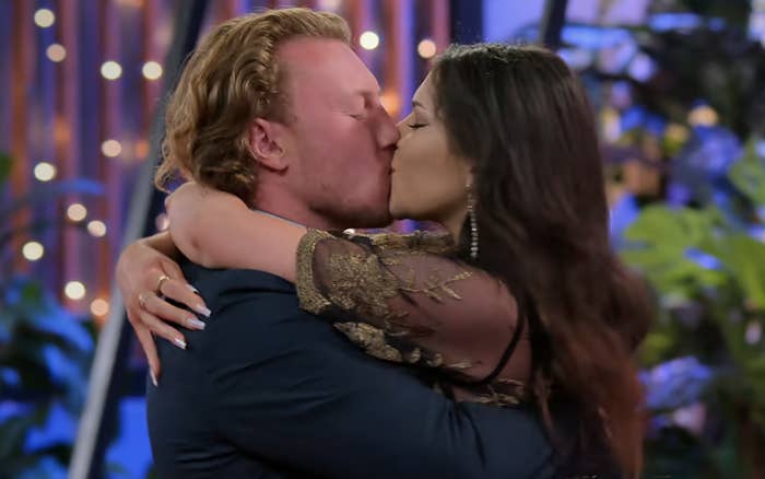 Two people embracing and kissing, with a blurred background of string lights