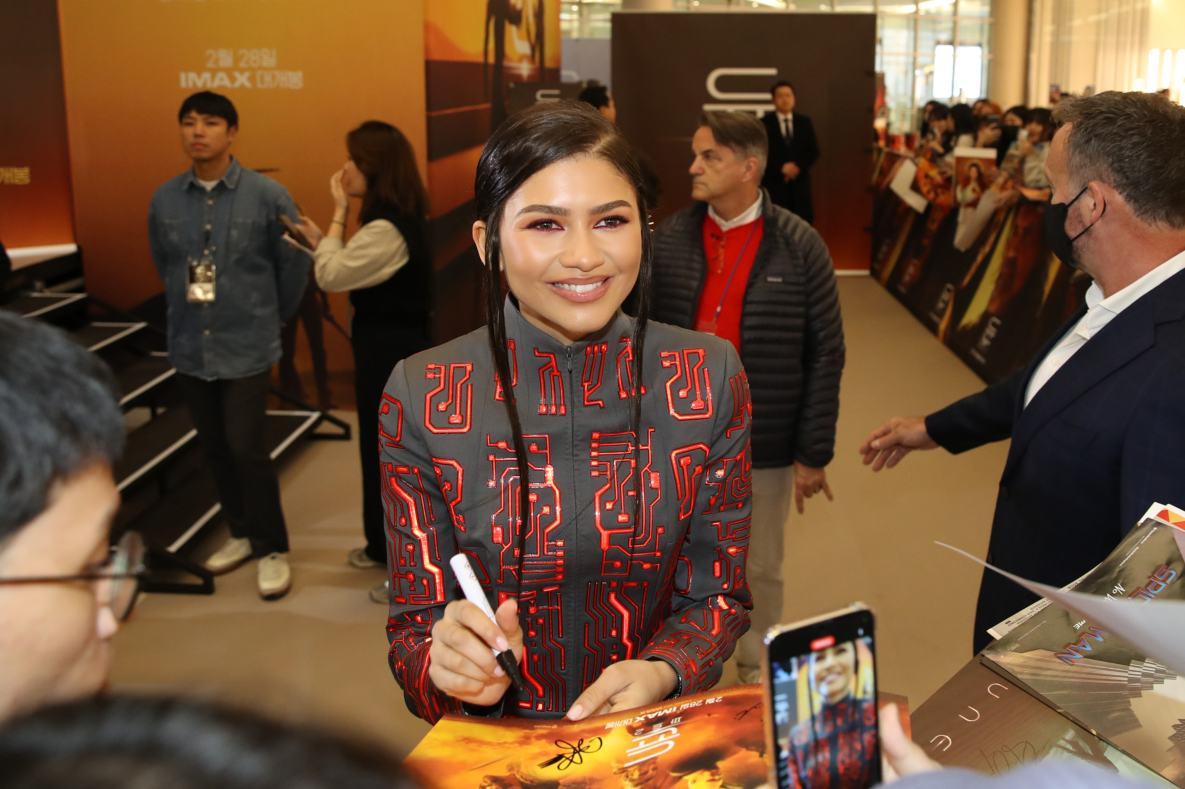 Zendaya smiles, signing autographs in a patterned jacket at an event