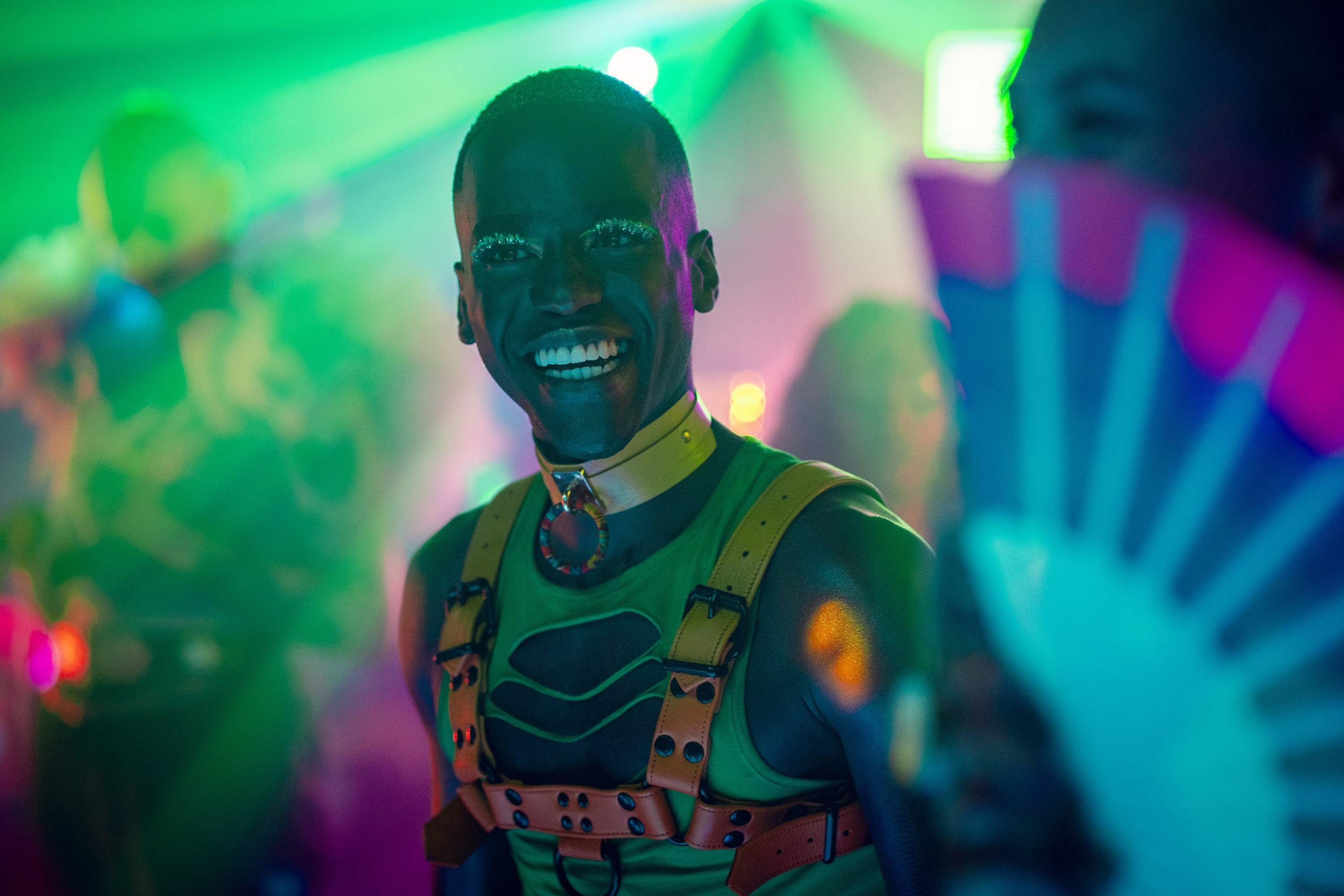 Eric with a beaming smile wearing futuristic attire and bold eye makeup at a club
